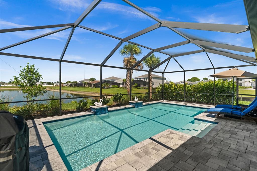 A screened-in swimming pool overlooks a lake with palm trees and houses in the background — 15620 NORTHRIDGE ROAD, PUNTA GORDA, FL