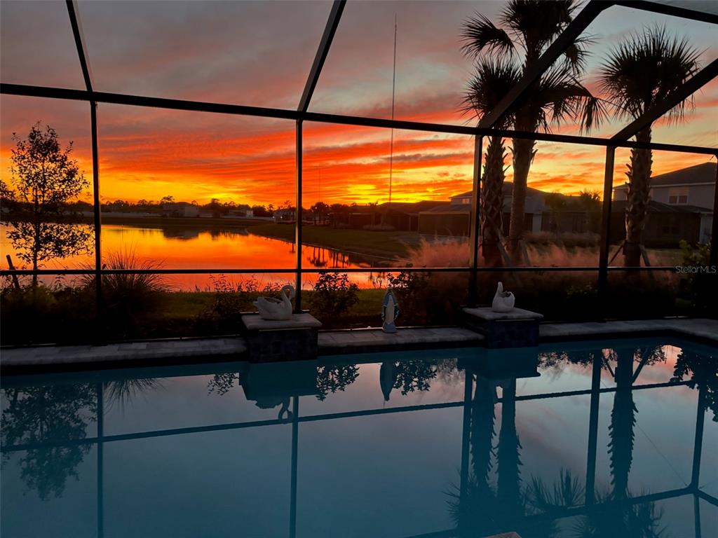 A swimming pool overlooks a lake at sunset through a screened-in lanai enclosure — 15620 NORTHRIDGE ROAD, PUNTA GORDA, FL