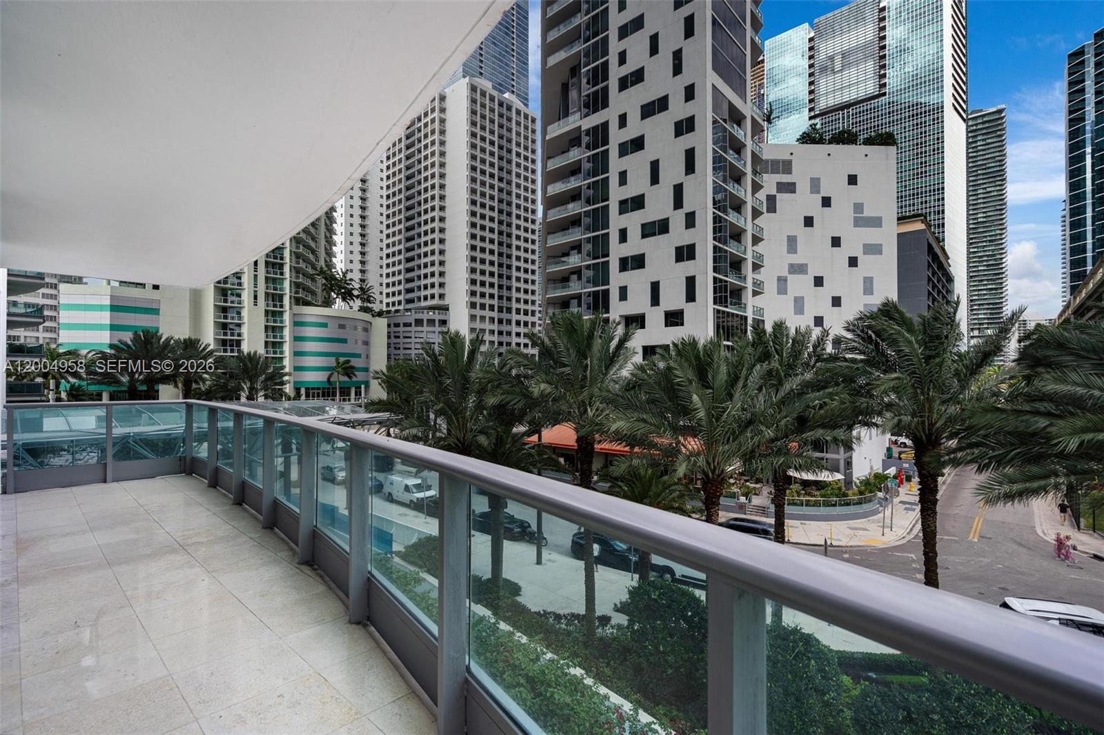A balcony with a glass railing overlooks a city street lined with palm trees and skyscrapers — 1331 Brickell Bay Dr # 302, Miami FL 33131, MIAMI, FL