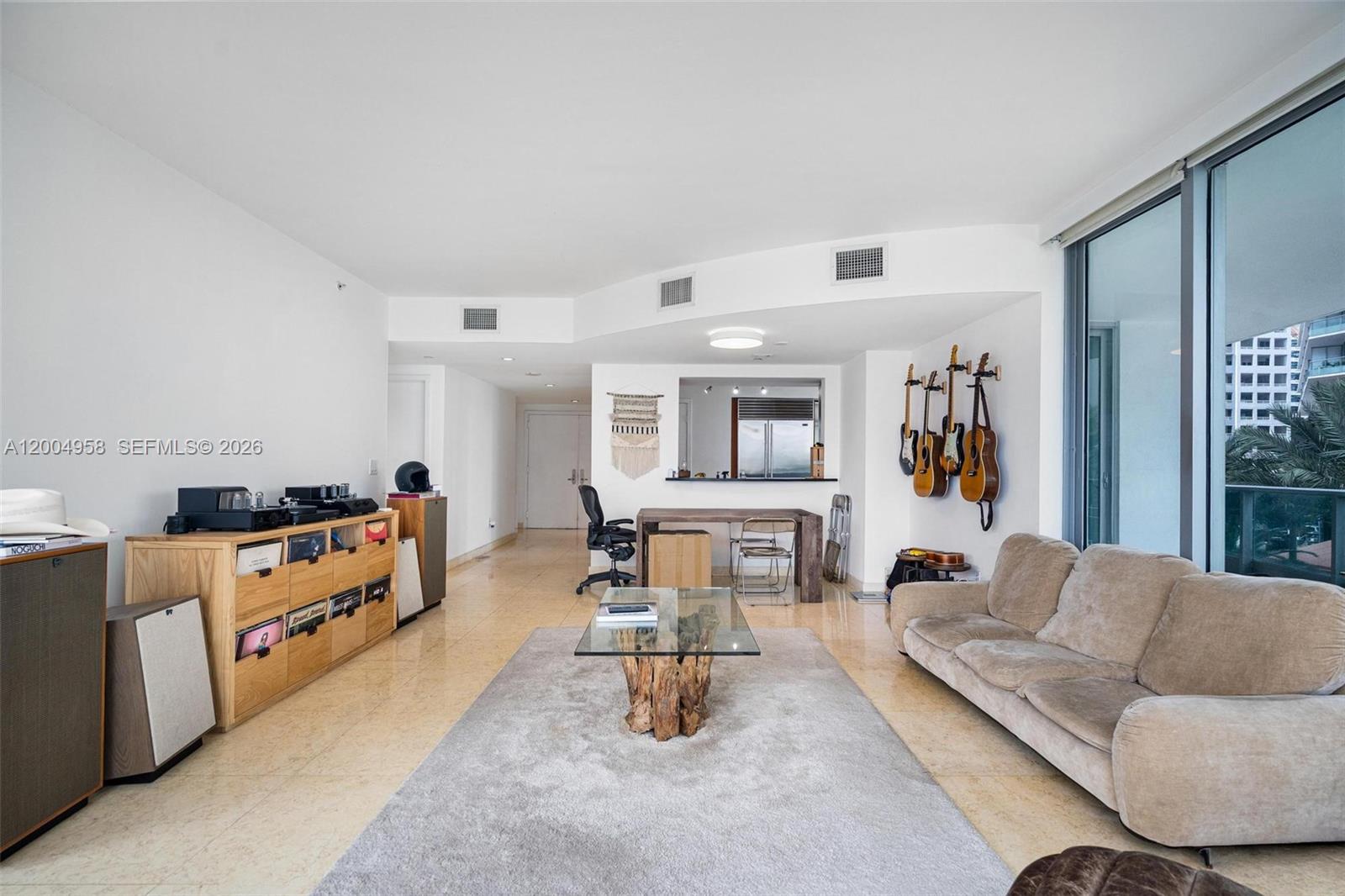 A living room features a beige sofa, a glass coffee table, and guitars on the wall — 1331 Brickell Bay Dr # 302, Miami FL 33131, MIAMI, FL