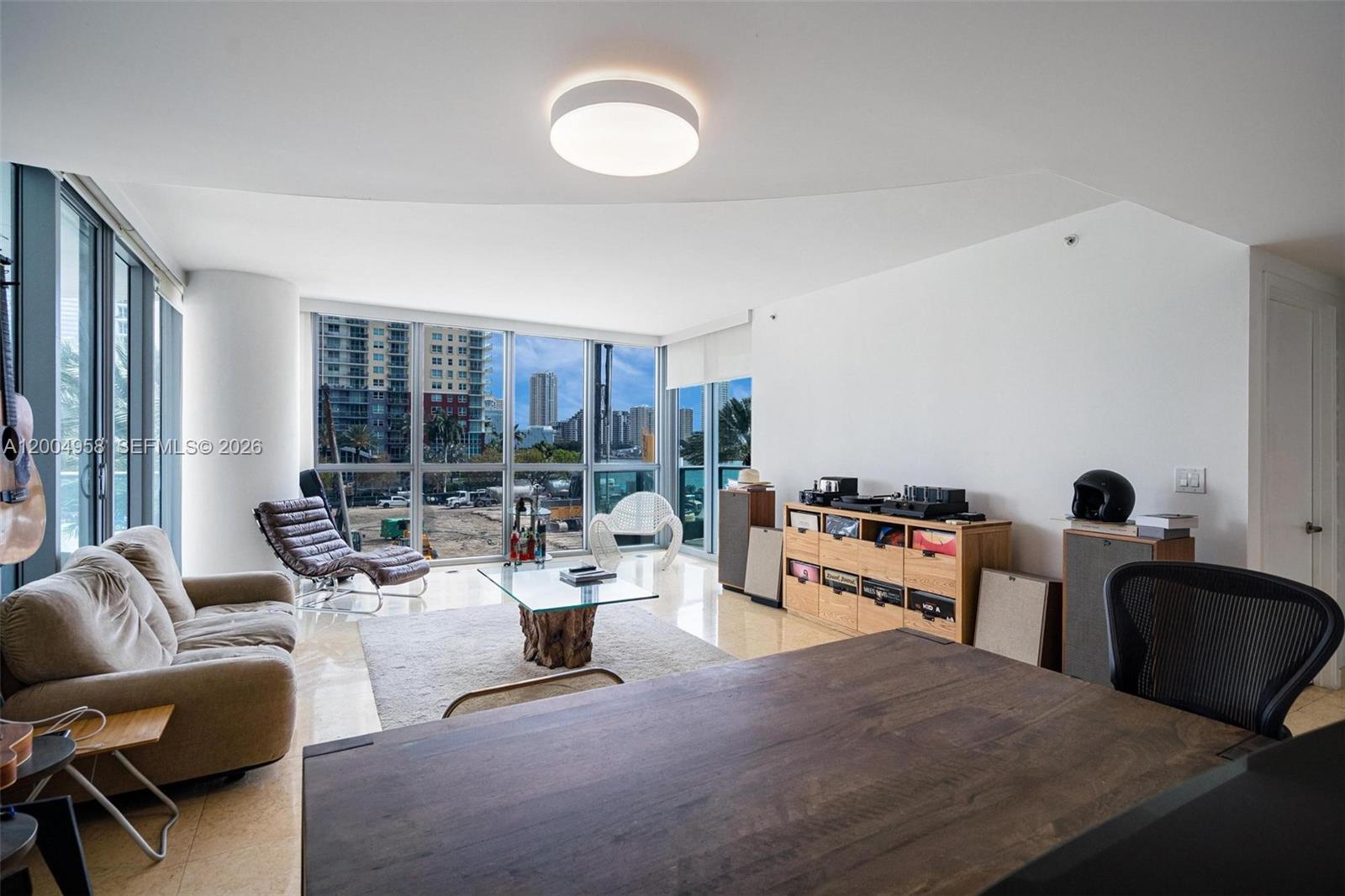 A modern living room features floor-to-ceiling windows, a beige sofa, and a wooden media console — 1331 Brickell Bay Dr # 302, Miami FL 33131, MIAMI, FL