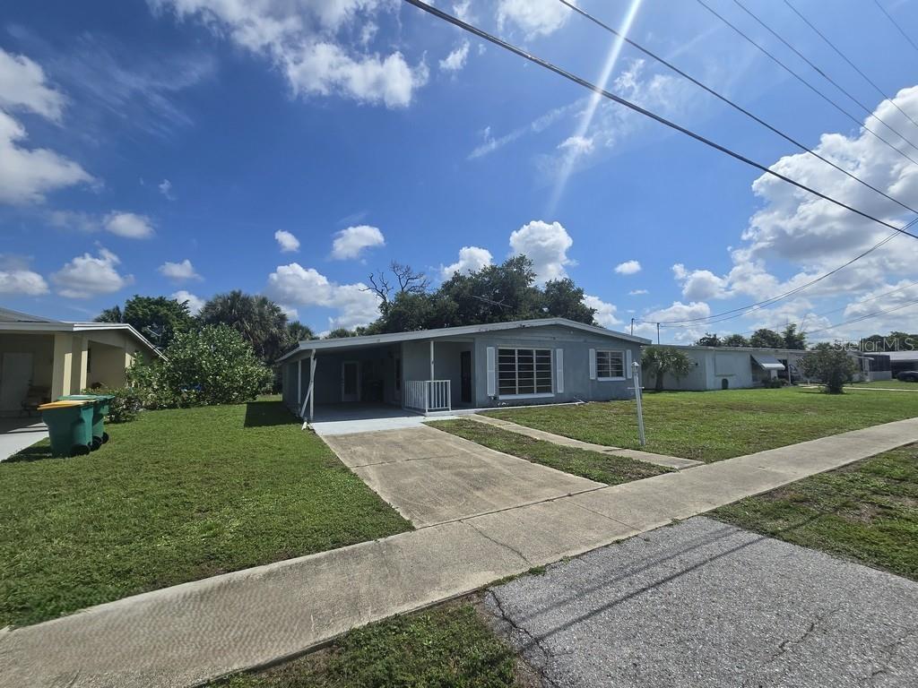 A single-story house with a concrete driveway, carport, and green lawn under a blue sky — 21330 HEPNER AVENUE, PORT CHARLOTTE, FL