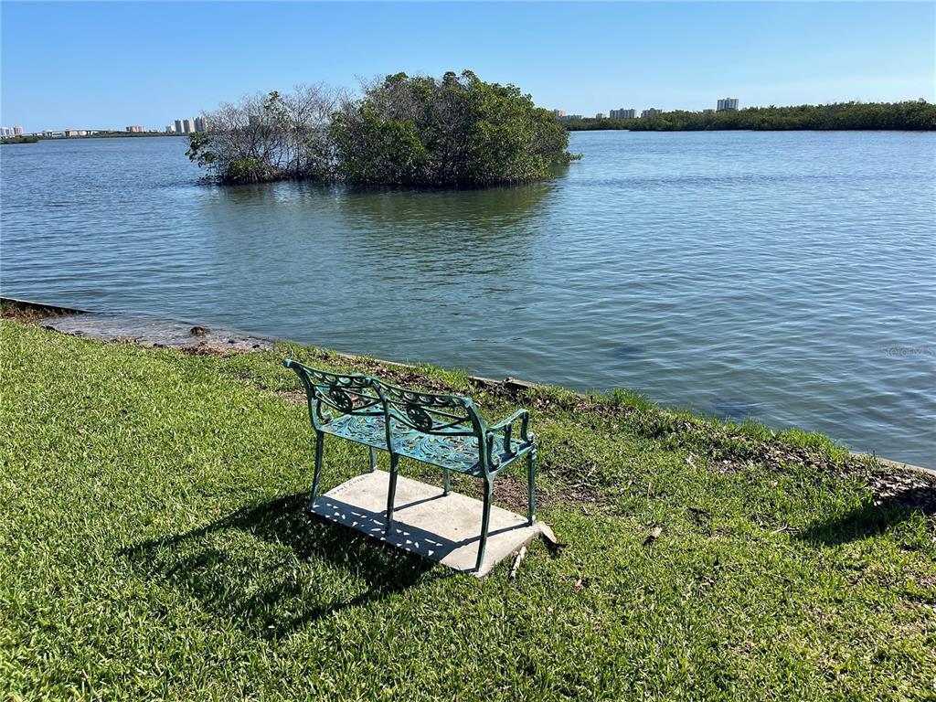 A metal bench sits on a grassy lawn overlooking a body of water with mangroves — 5242 RIVERSIDE DRIVE, PORT ORANGE, FL