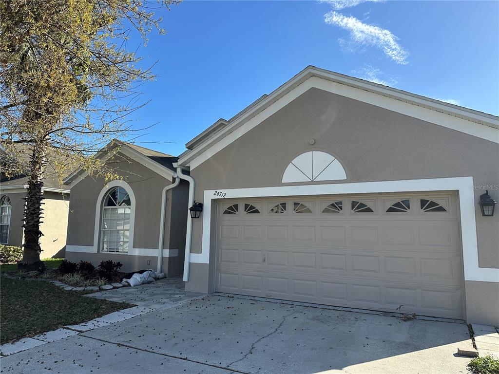 A tan, single-story house features a two-car garage, a front arched window, and a palm tree — 24712 PORTOFINO DRIVE, LUTZ, FL