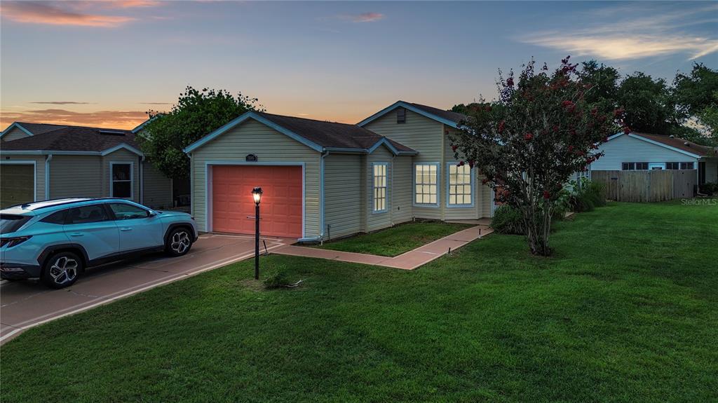 A light yellow house with a coral garage door and a blue SUV parked outside — 25345 GREEN HERON DRIVE, LEESBURG, FL