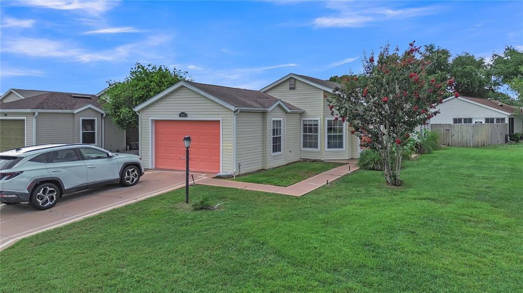 A light-colored single-story house with a coral garage door and a white SUV parked outside — 25345 GREEN HERON DRIVE, LEESBURG, FL