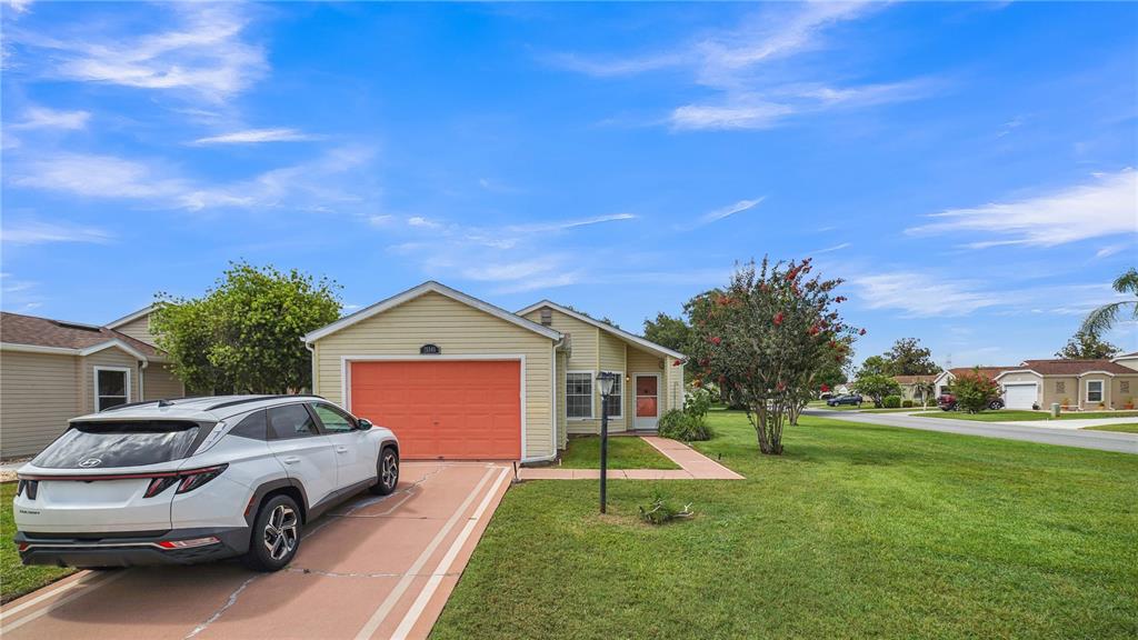 A single-story house with light yellow siding, an orange garage door, and a white car — 25345 GREEN HERON DRIVE, LEESBURG, FL