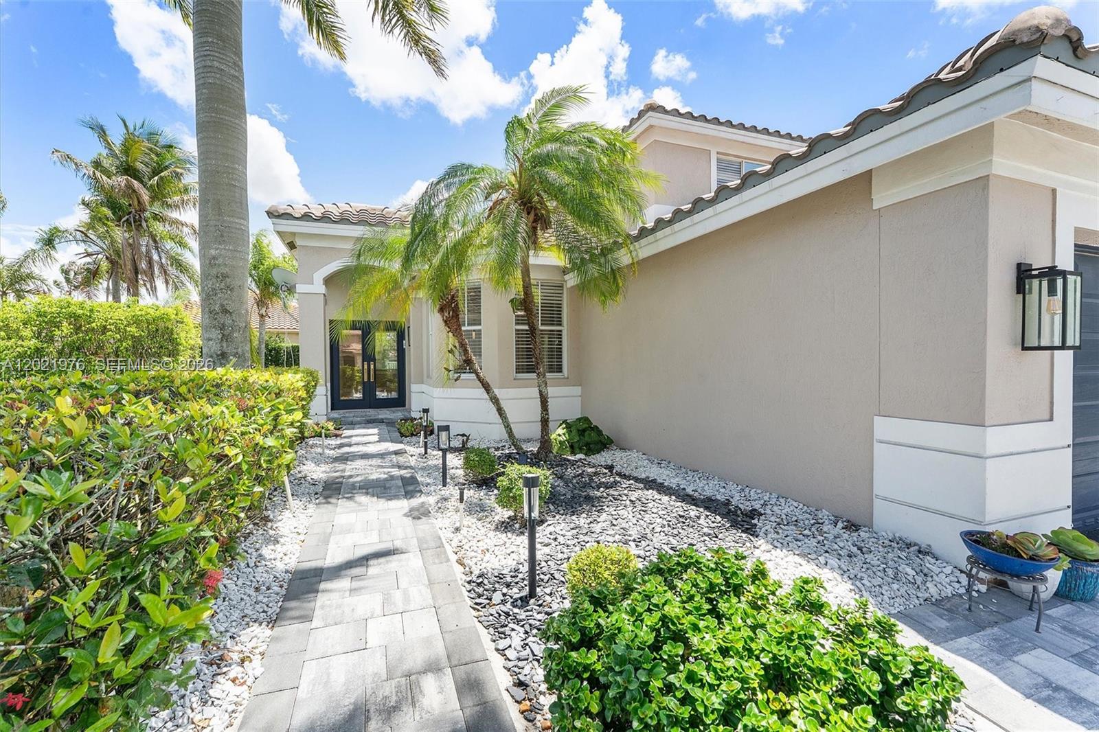 A paved walkway leads to the front entrance of a house with palm trees — 1868 Silverbell Ter, Weston FL 33327, WESTON, FL
