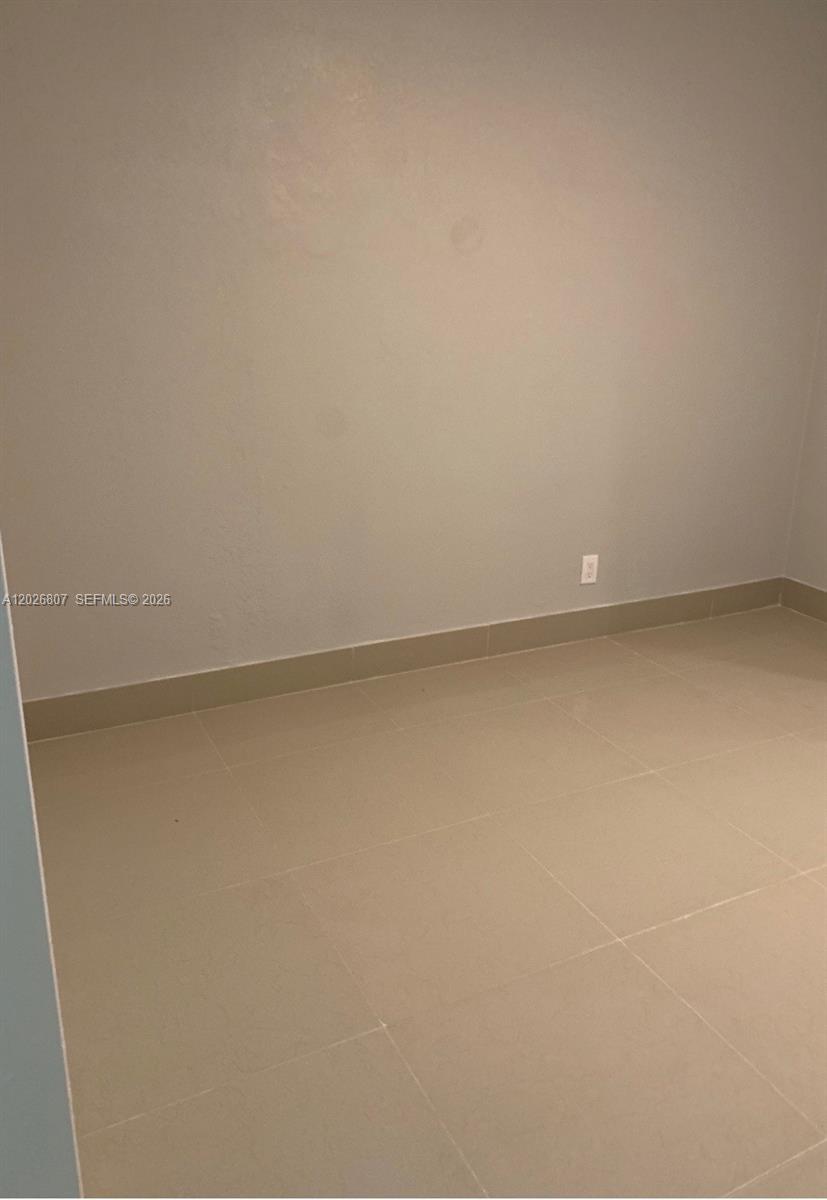 An empty room features light-colored walls, beige tile flooring, and a single electrical outlet — 6498 Collins Ave # 41, Miami Beach FL 33141, MIAMI BEACH, FL