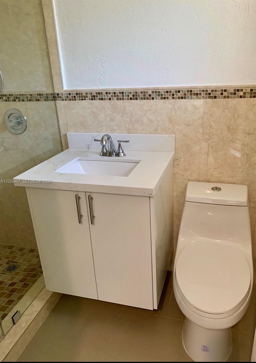 A bathroom features a white vanity with a marble countertop, a toilet, and tiled walls — 6498 Collins Ave # 41, Miami Beach FL 33141, MIAMI BEACH, FL