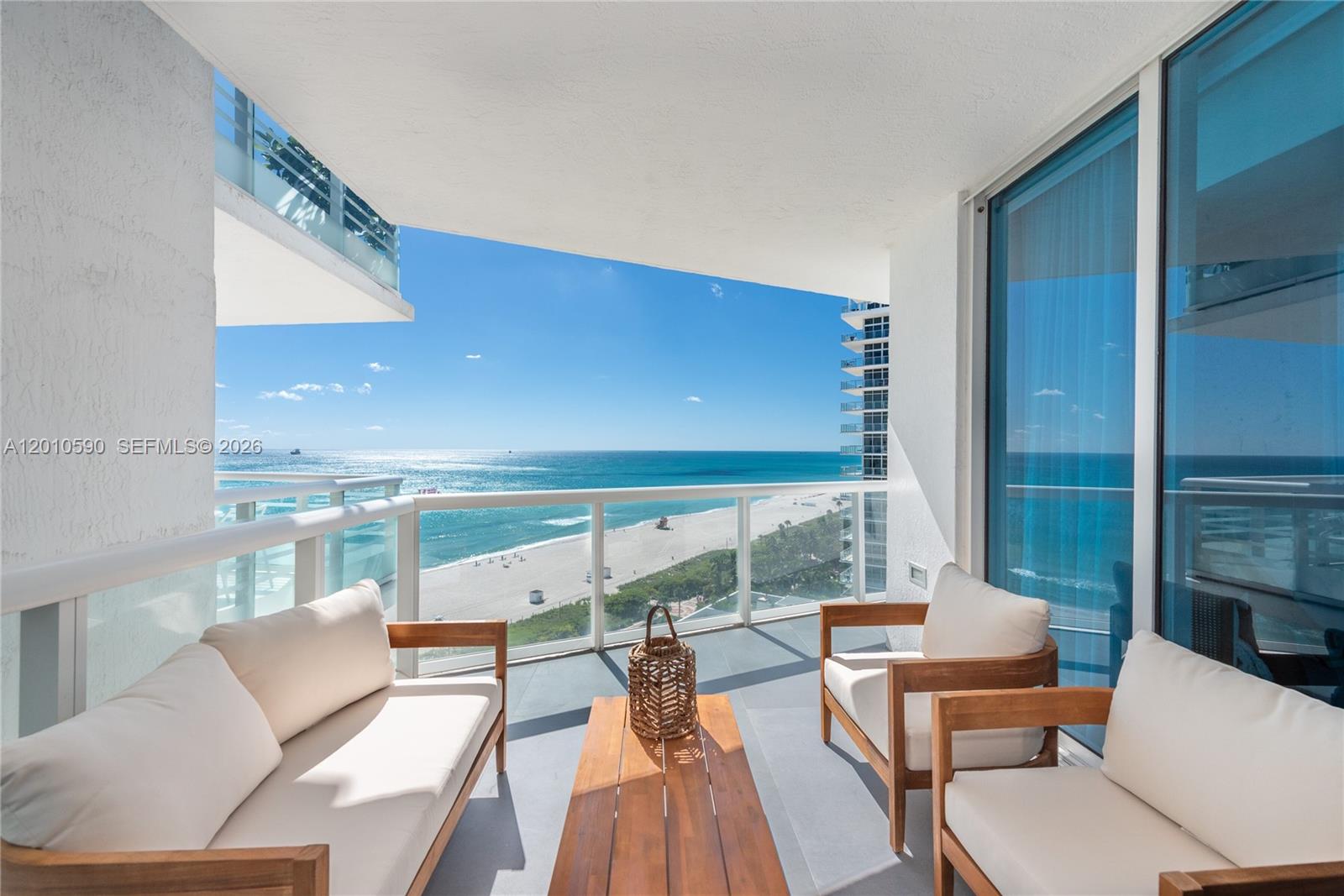 A balcony with wooden furniture overlooks the ocean and a sandy beach — 3801 Collins Ave # 1502, Miami Beach FL 33140, MIAMI BEACH, FL