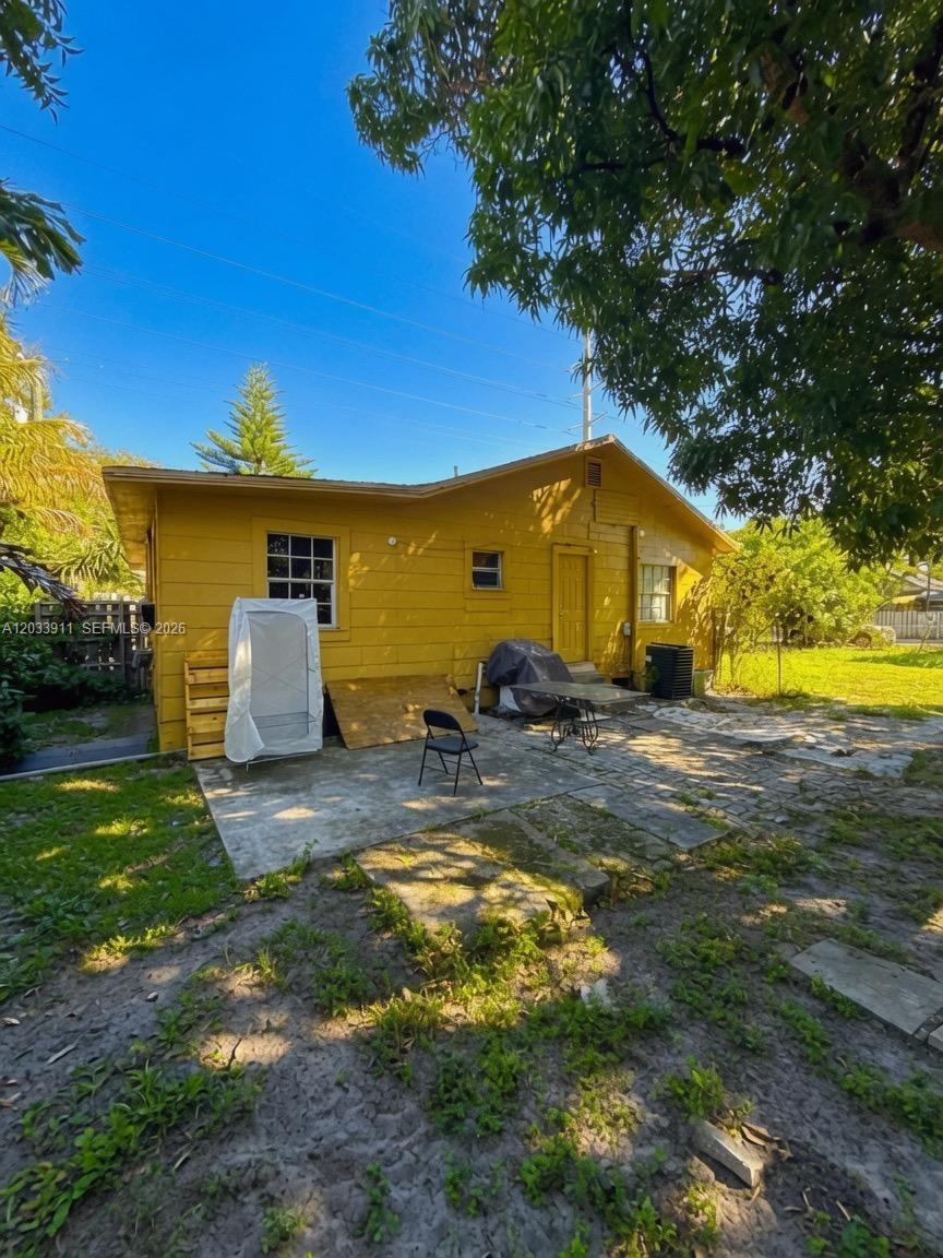 The exterior of a yellow house features a concrete patio, a door, and windows — 1100 N 24th Ave, Hollywood FL 33020, HOLLYWOOD, FL