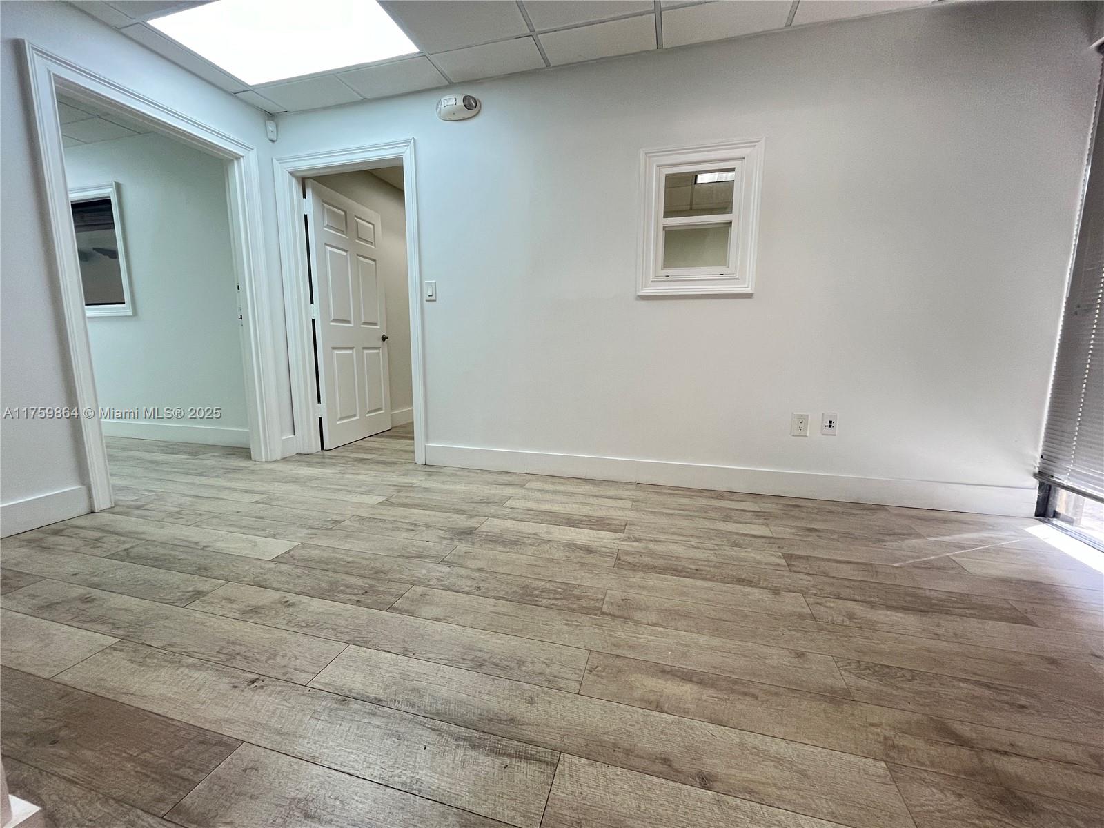 An office room with light wood-look flooring, white walls, two doorways, and a small window — 4350 NW 19th Ave # C, Deerfield Beach FL 33064, DEERFIELD BEACH, FL