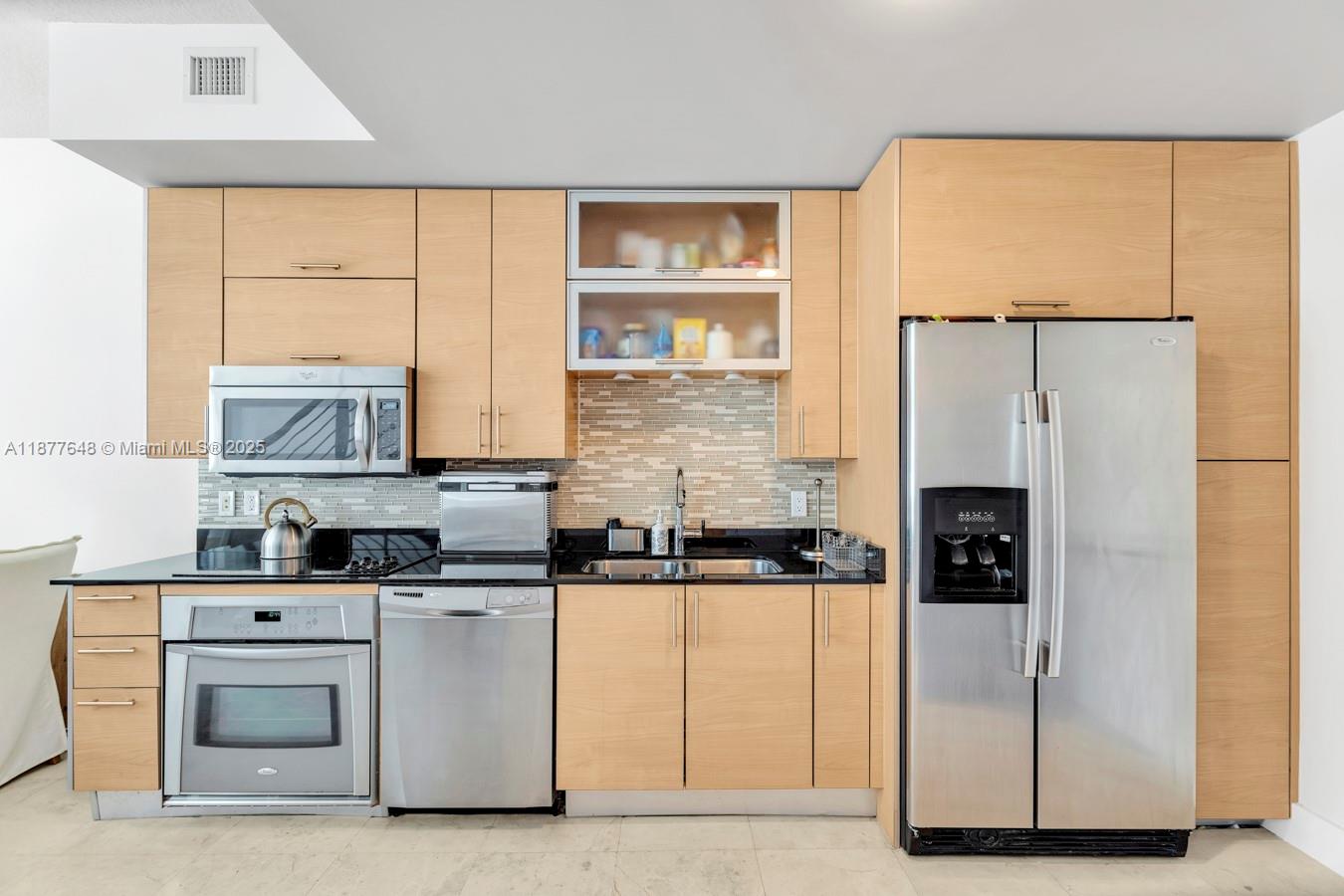A kitchen features light wood cabinetry, stainless steel appliances, and a tiled backsplash — 60 SW 13th St # 3402, Miami FL 33130, MIAMI, FL