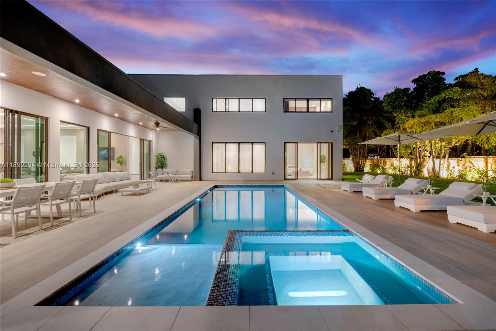 A modern two-story house features a swimming pool, hot tub, and patio at dusk — 2110 NE 197th Ter, Miami FL 33179, MIAMI, FL