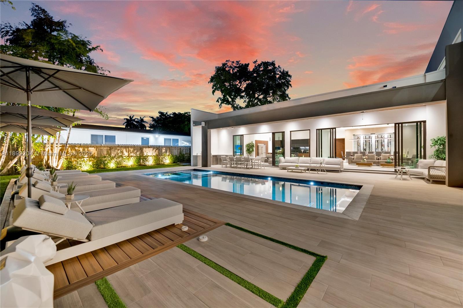 A modern patio features a swimming pool, lounge chairs, and a sunset sky — 2110 NE 197th Ter, Miami FL 33179, MIAMI, FL