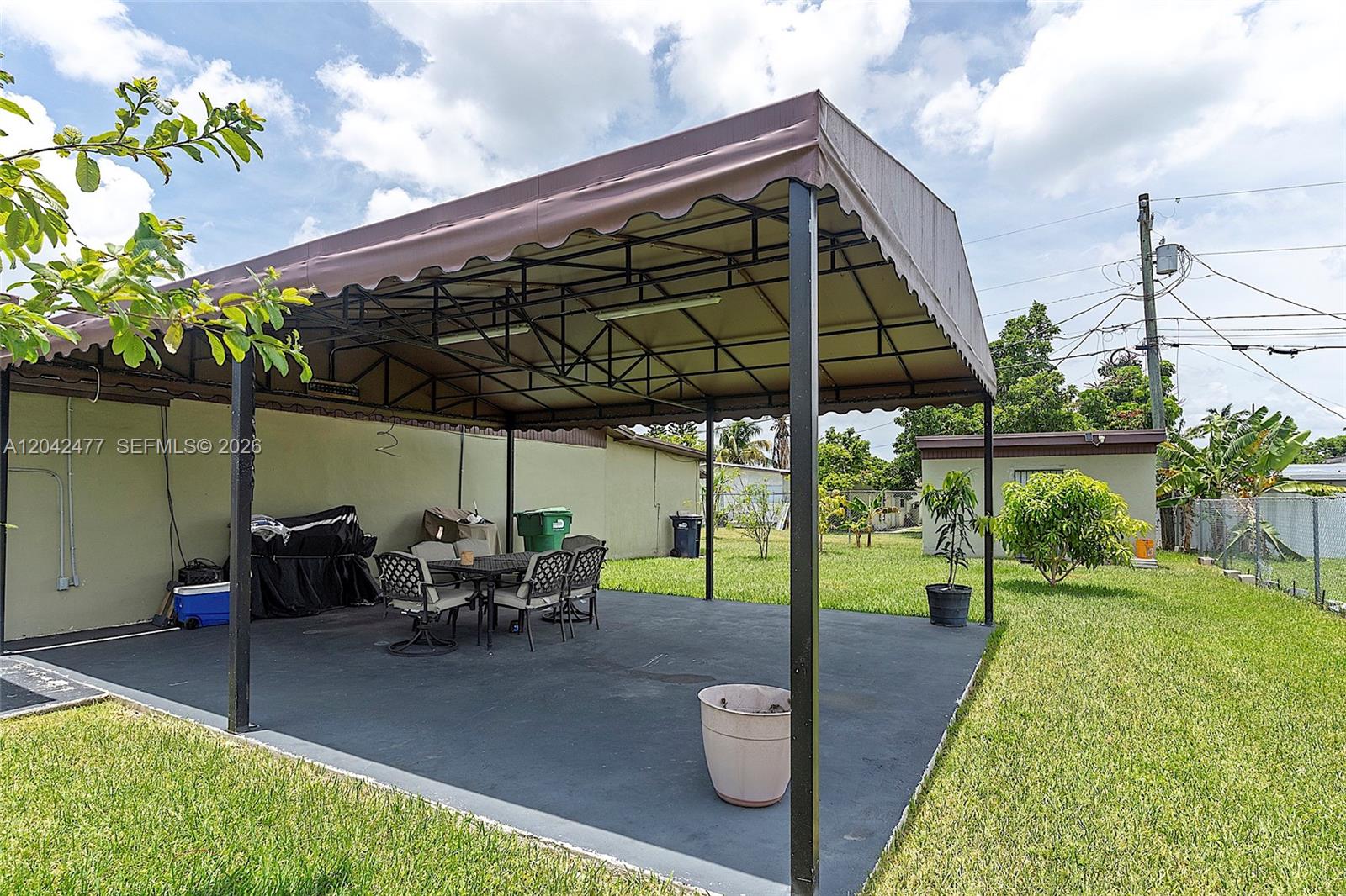 A covered patio with a metal frame and fabric awning sits on a concrete slab — HOMESTEAD, FL