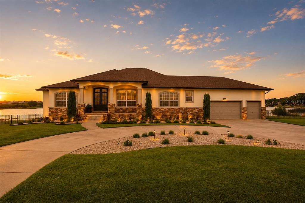 A single-story house with a stone facade, arched windows, and a three-car garage at sunset — 5911 OLD BERKLEY ROAD, AUBURNDALE, FL