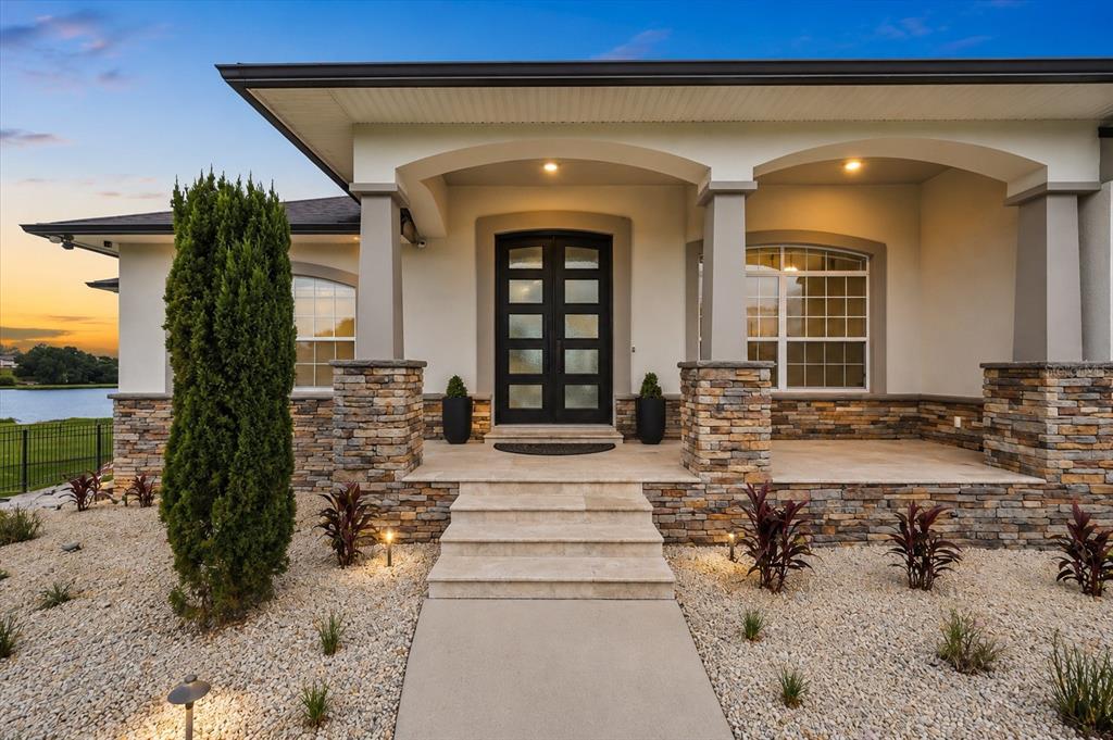 A stone-accented house exterior features a covered porch, double front doors, and a gravel yard — 5911 OLD BERKLEY ROAD, AUBURNDALE, FL