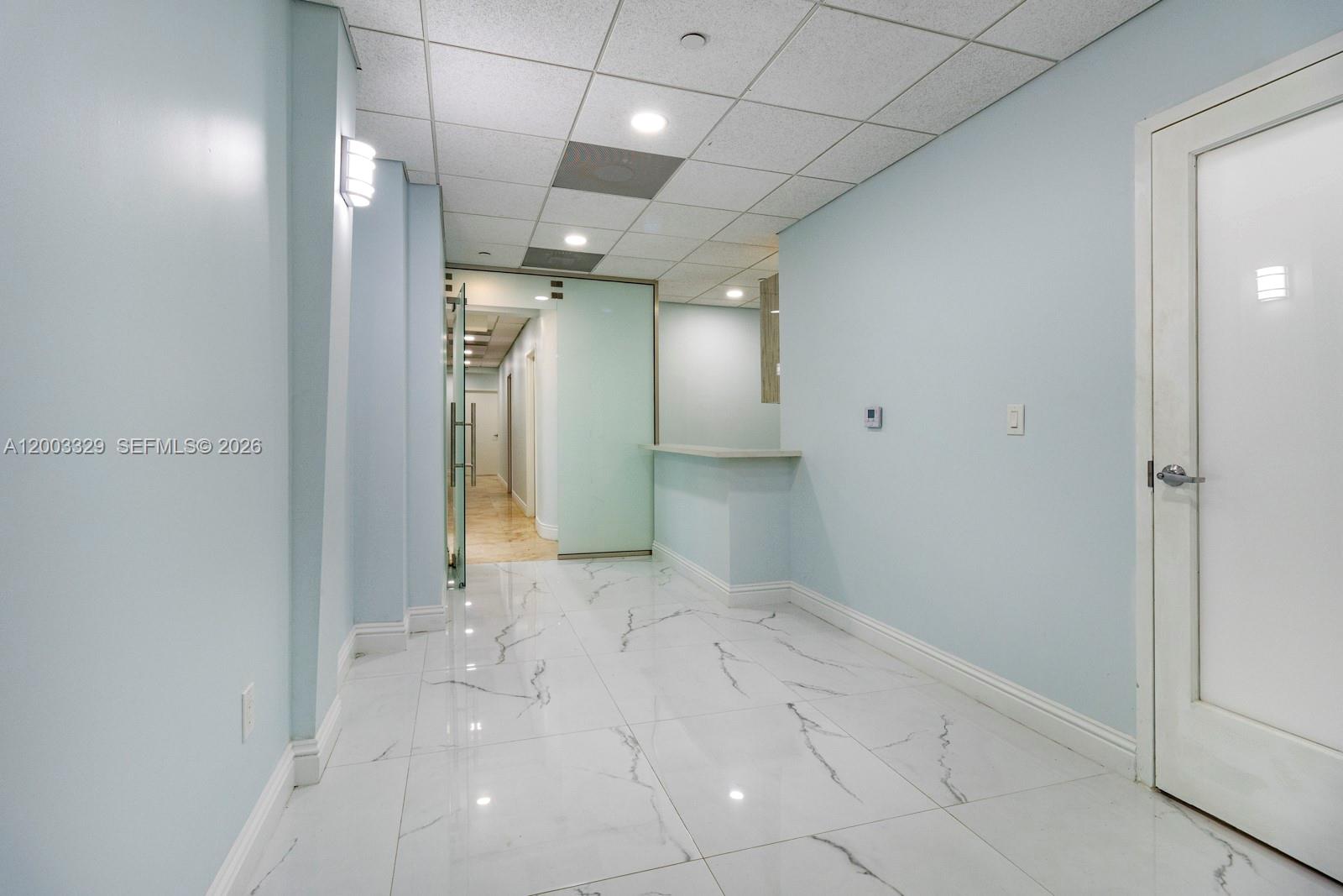 A hallway with light blue walls, white marble-style tile flooring, and a glass-paneled door — 6141 Sunset Dr # 102, South Miami FL 33143, SOUTH MIAMI, FL