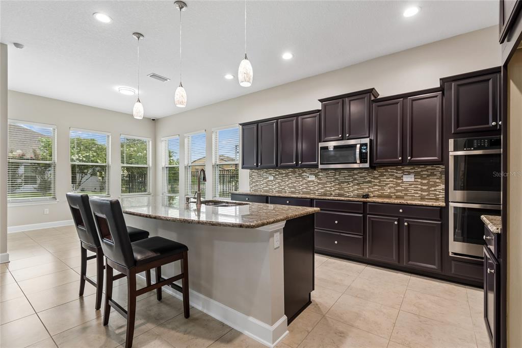 A kitchen features dark wood cabinets, granite countertops, a center island, and stainless steel appliances — 4930 BUTLER NATIONAL DRIVE, WESLEY CHAPEL, FL