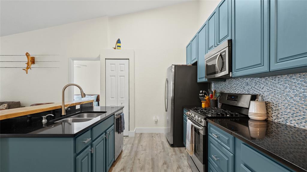 A kitchen features blue cabinets, black countertops, stainless steel appliances, and a mosaic tile backsplash — 13810 SUTTON PARK DRIVE N UNIT 1336, JACKSONVILLE, FL