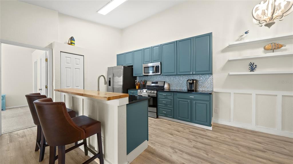 A kitchen features blue cabinets, a wooden breakfast bar, and white floating shelves — 13810 SUTTON PARK DRIVE N UNIT 1336, JACKSONVILLE, FL