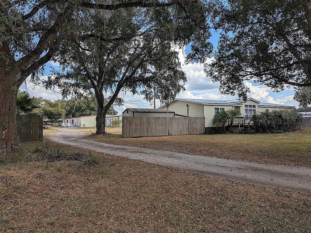 A light-colored manufactured home sits behind a wooden fence next to a dirt driveway — 4402 GALLAGHER ROAD, PLANT CITY, FL