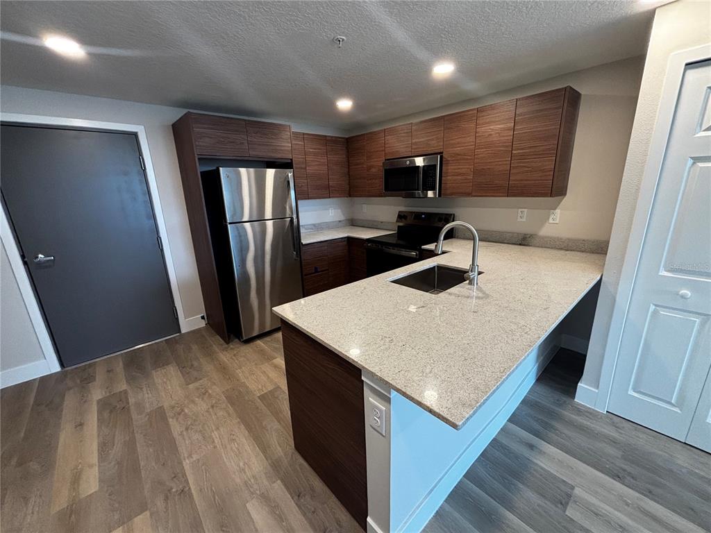 A modern kitchen features wood-grain cabinets, stainless steel appliances, and a granite-topped island — 4424 S TEXAS AVENUE UNIT 314, ORLANDO, FL