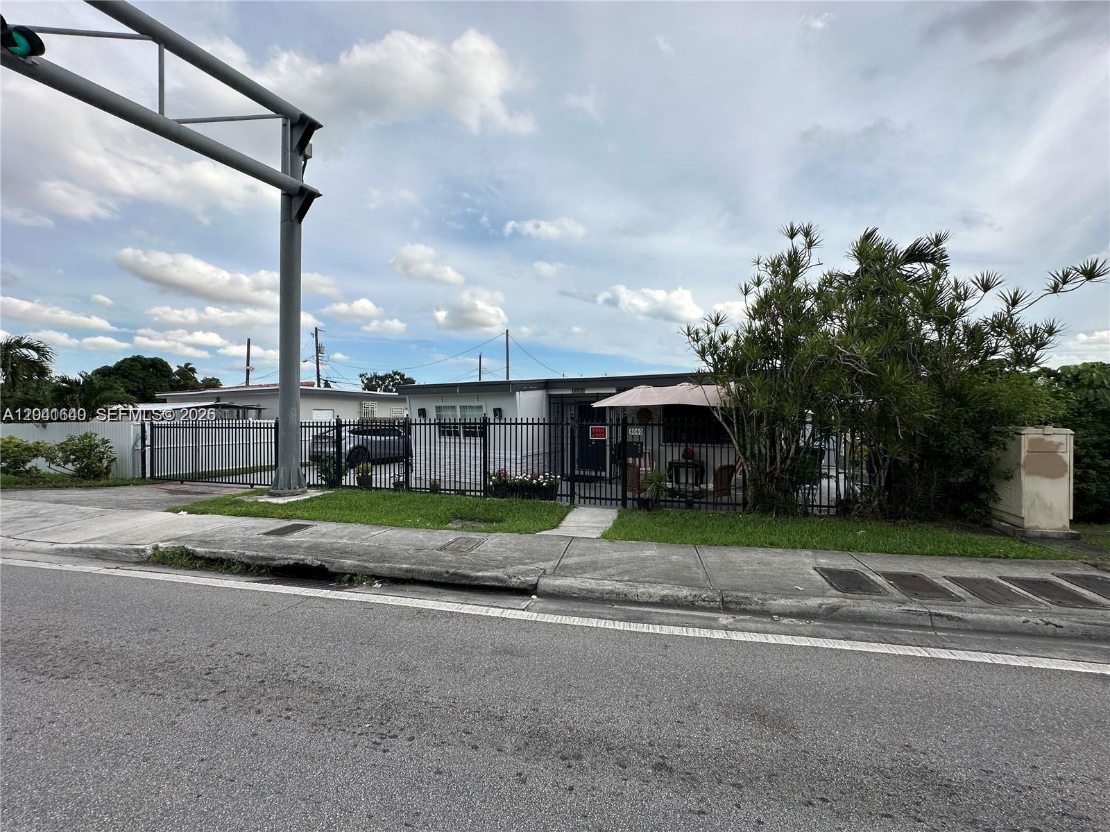 A single-story house with a fenced front yard and an umbrella sits along a street — 6060 NW 7th St, Miami FL 33126, MIAMI, FL