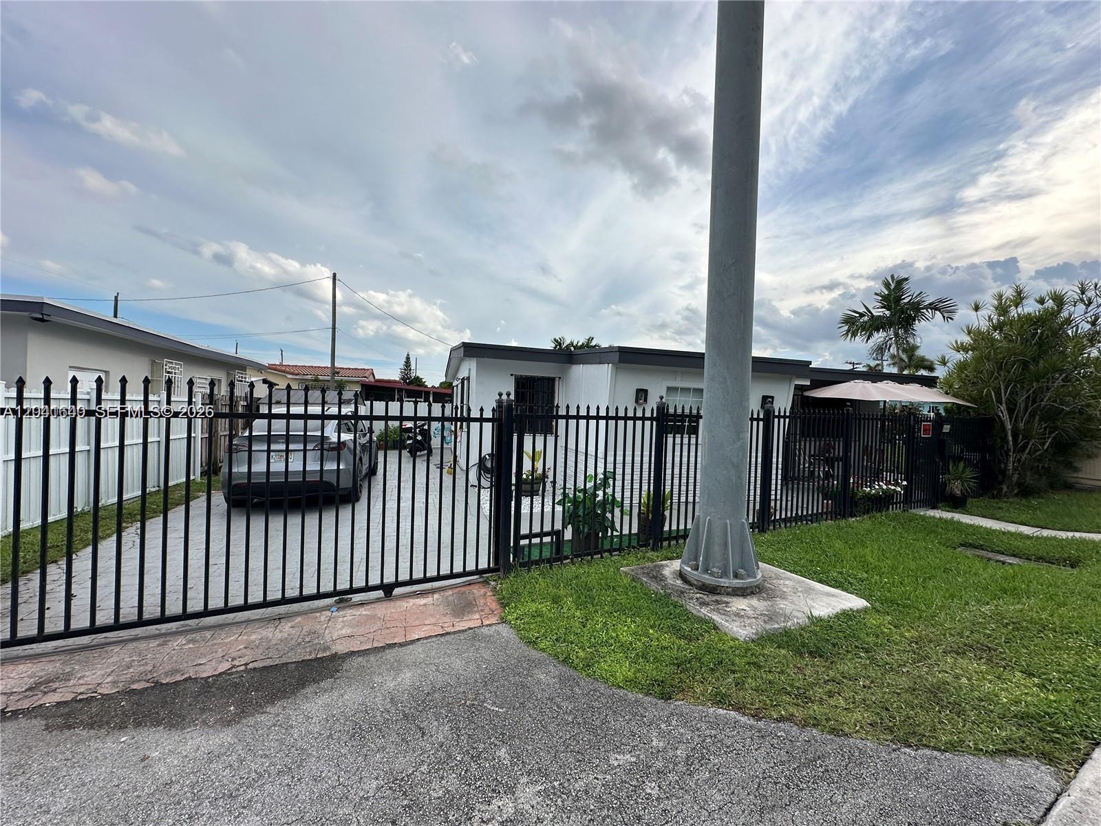 A white house with a paved driveway is enclosed by a black metal fence — 6060 NW 7th St, Miami FL 33126, MIAMI, FL