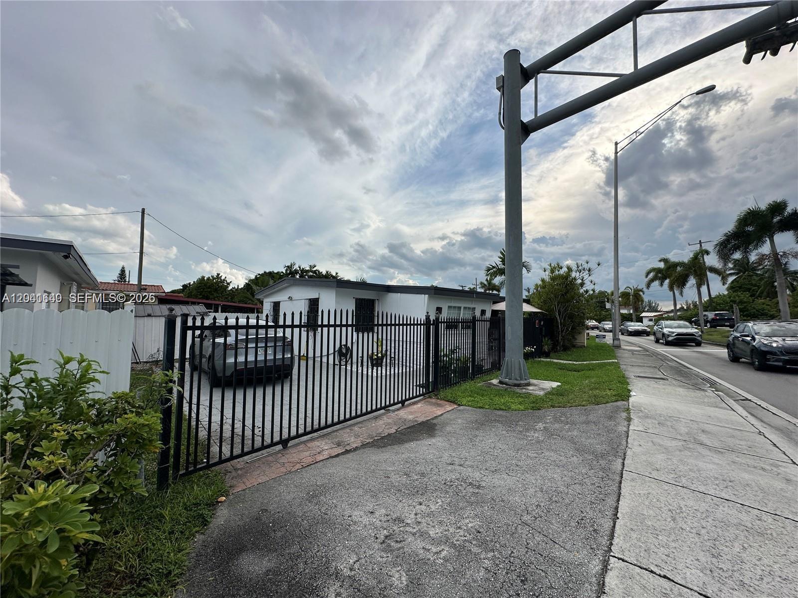 A white house with a black metal fence and gate sits beside a paved road — 6060 NW 7th St, Miami FL 33126, MIAMI, FL