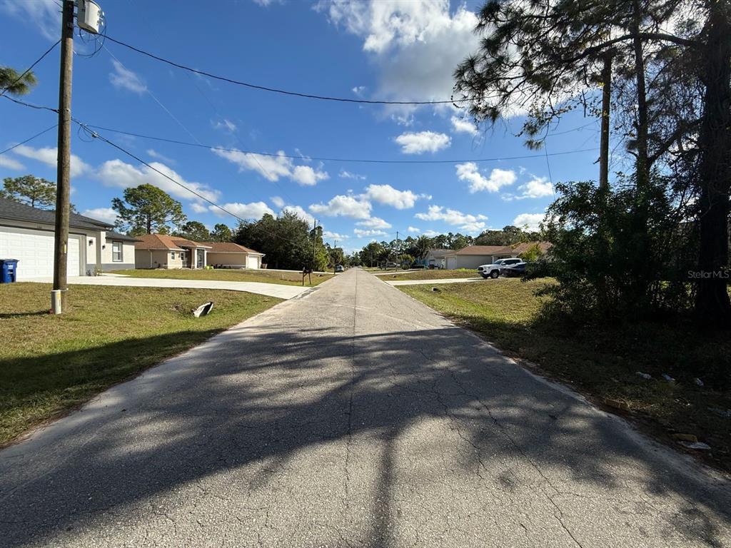 A paved residential street stretches between houses under a blue sky with scattered clouds — 3315 24TH STREET W, LEHIGH ACRES, FL