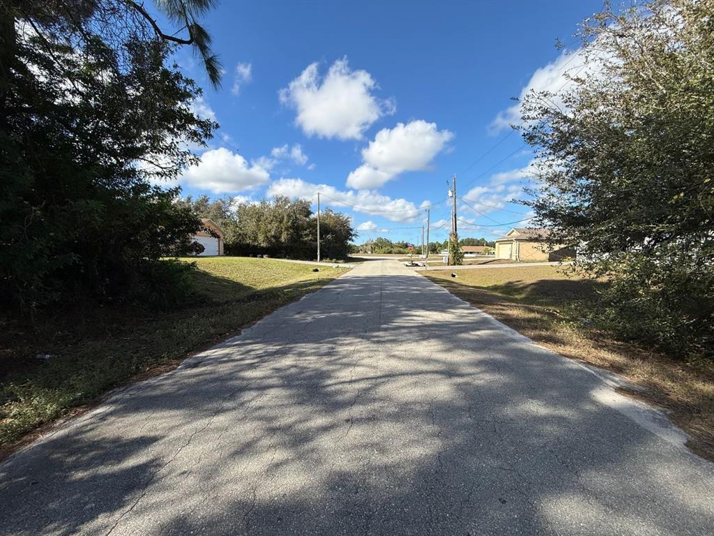 A paved residential street leads toward a distant intersection under a bright, partly cloudy sky — 3315 24TH STREET W, LEHIGH ACRES, FL