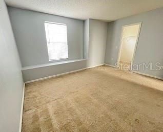 An empty bedroom features light blue walls, beige carpeting, a window, and a walk-in closet — 1407 NELSON BROOK WAY, KISSIMMEE, FL