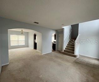 A carpeted living room features an arched entryway, a staircase, and a view into the kitchen — 1407 NELSON BROOK WAY, KISSIMMEE, FL