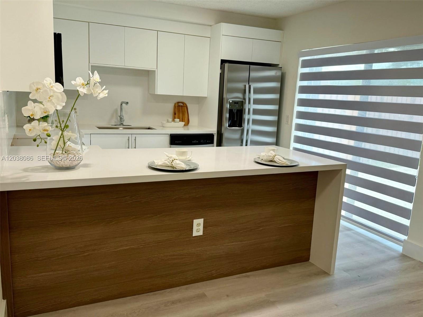A modern kitchen features white cabinetry, stainless steel appliances, and a wood-paneled breakfast bar — 2565 Garden Ct, Cooper City FL 33026, COOPER CITY, FL