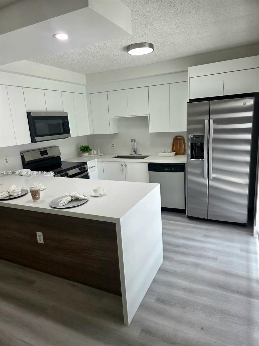 A modern kitchen features white cabinetry, stainless steel appliances, and a wood-paneled island — 2565 Garden Ct, Cooper City FL 33026, COOPER CITY, FL