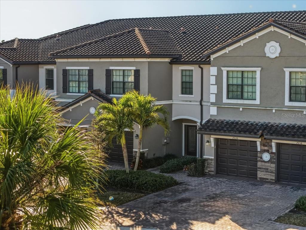 A multi-story townhouse exterior features a tiled roof, brown garage doors, and a paved driveway — 7224 KETCH PLACE, BRADENTON, FL