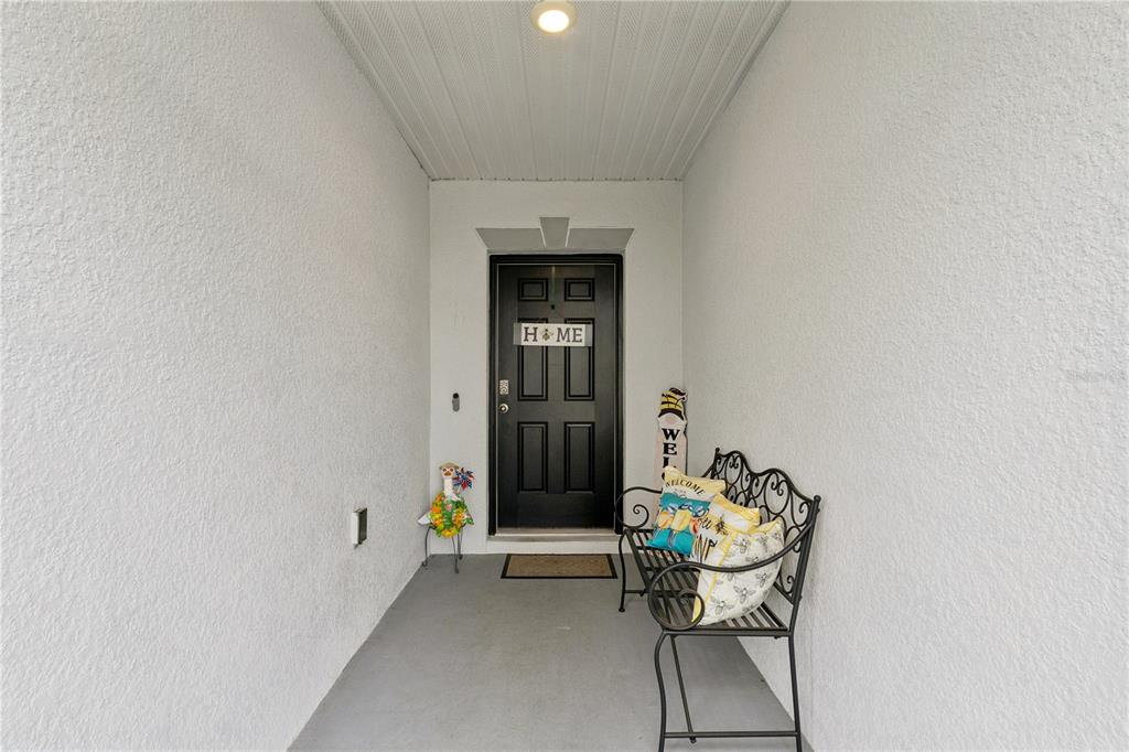 A covered entryway features a black front door, a metal bench, and white stucco walls — 15280 WHITE TAIL LOOP, MASCOTTE, FL