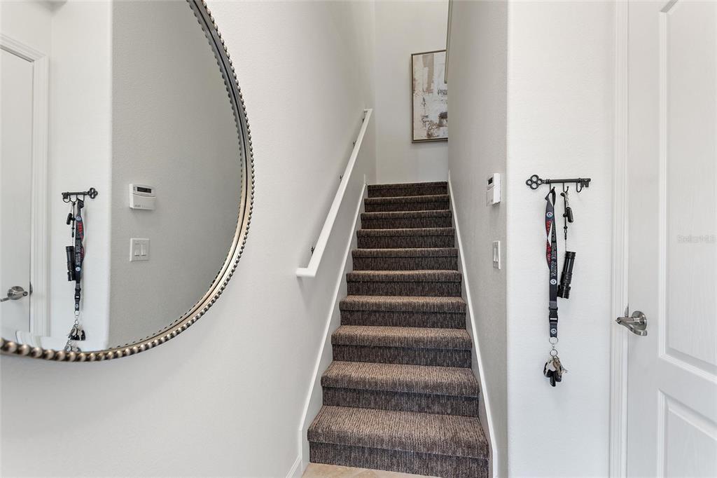 A carpeted staircase leads upward between two white walls with a mirror and key hooks — 8928 AZALEA SANDS LN UNIT 8928, DAVENPORT, FL