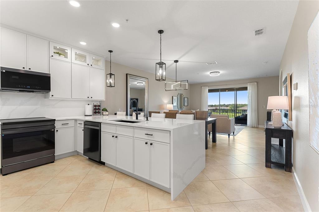 A modern kitchen with white cabinets and a large island overlooks an open living area — 8928 AZALEA SANDS LN UNIT 8928, DAVENPORT, FL