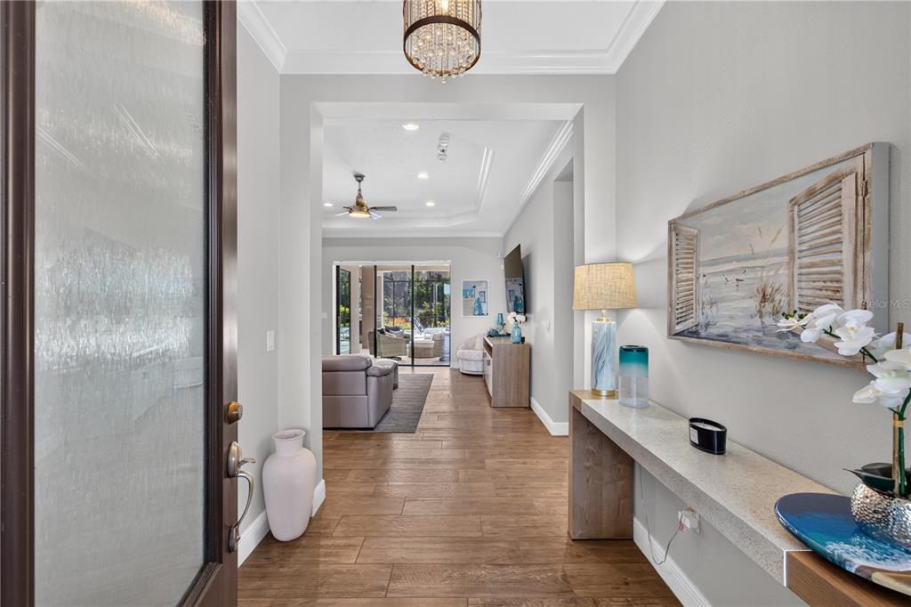 A bright entryway features wood-look tile flooring, a crystal chandelier, and a console table — 8276 LARKSPUR CIRCLE, SARASOTA, FL
