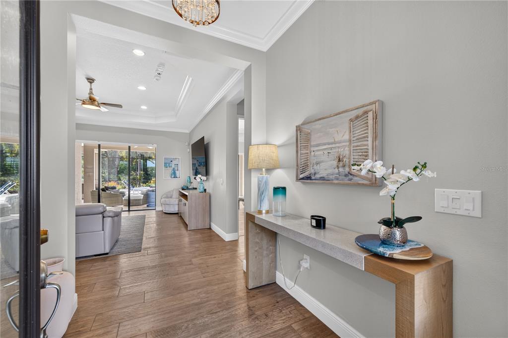 A foyer with wood-look tile flooring leads into a living room with a tray ceiling — 8276 LARKSPUR CIRCLE, SARASOTA, FL