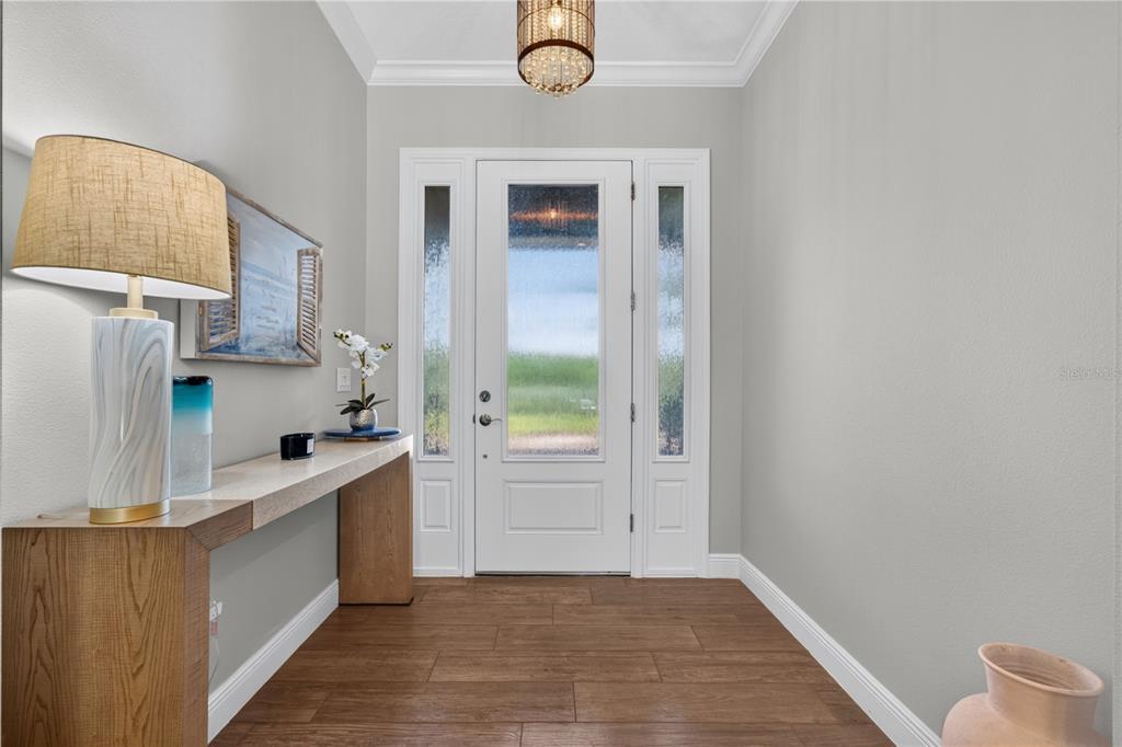 An entryway features a wood console table, a lamp, a chandelier, and a glass-paneled front door — 8276 LARKSPUR CIRCLE, SARASOTA, FL