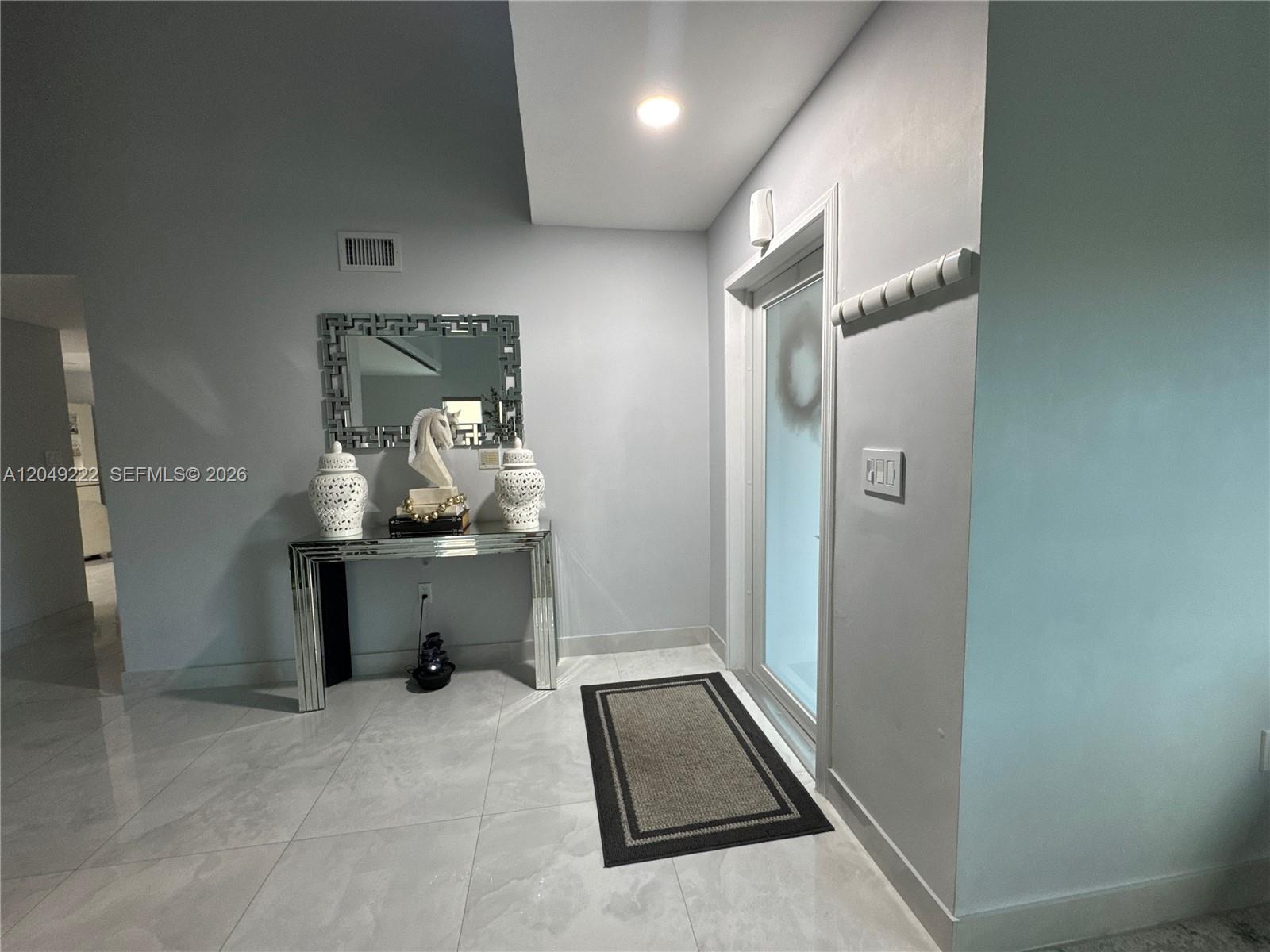 A modern entryway features a mirrored console table, a decorative mirror, and light-colored tile flooring — 9368 SW 146th Pl # 0, Miami FL 33186, MIAMI, FL