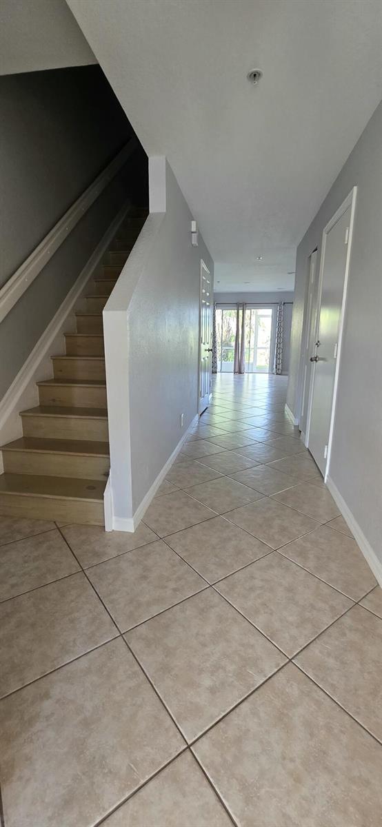 A hallway with light-colored tile flooring leads toward a glass door with stairs on the left — 5357 SE Jennings Lane, Stuart FL 34997, STUART, FL