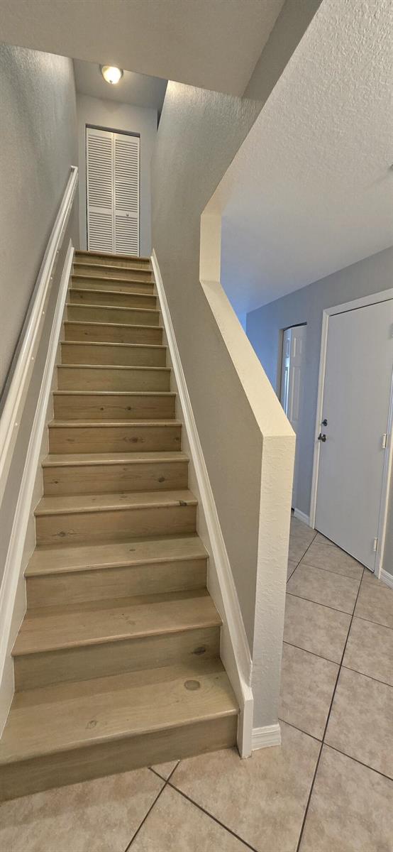 A staircase with light wood treads leads upward next to a tiled entryway and door — 5357 SE Jennings Lane, Stuart FL 34997, STUART, FL