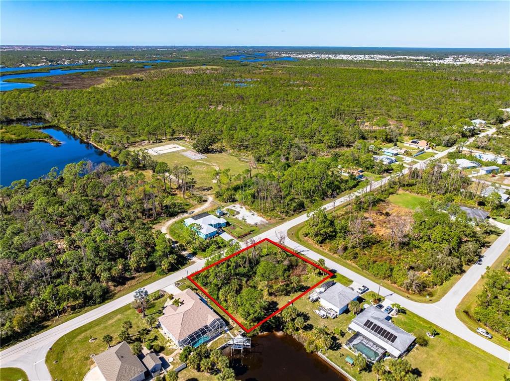 An aerial view shows a vacant, wooded lot outlined in red next to a waterfront home — 1096 CAMPBELL STREET, PORT CHARLOTTE, FL