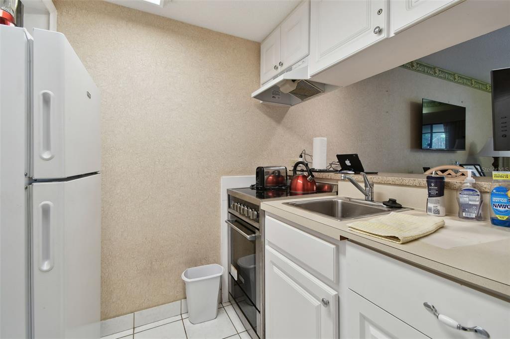 A small kitchen features white cabinets, a white refrigerator, and a stainless steel sink — 36750 US HIGHWAY 19 N UNIT 09208, PALM HARBOR, FL